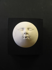 Photo of round white ceramic head with impressed stars and other symbols. Mounted on 3.5 square black wood