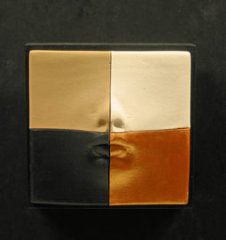 Small ceramic white face divided into squares. One square is natural white the other 3 painted. Mounted on 3.5" black block