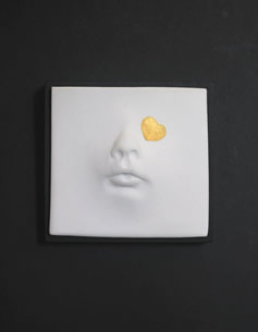 pure white ceramic wall piece with a face and one gold heard. Mounted on 3.5" black block.